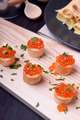 Crepes with red caviar on a wooden board sprinkled with parsley. Russian cuisine