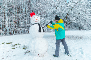 man making snowman outdoors at frosty winter park