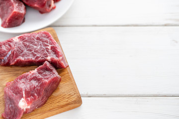 Raw meat. Raw fresh beef steak on a wood cutting board. White wooden background, top view, copy space, Daylight