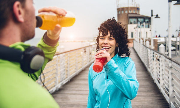Man And Woman Drinking Energy Drink From Bottle After Fitness Sport Exercise