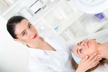 Female beautician doctor with patient in wellness center. Professional cosmetologist make procedure to beautiful girl in cosmetology cabinet or beauty parlor.
