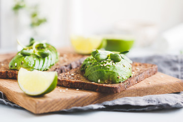 Two toasts with avocado on a wooden board on a breakfast table. The concept of vegetarian and healthy diet food.