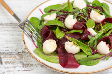 salad with beets and rucola and mozzarella cheese on a white wooden background