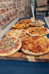 seven pizzas on a wooden board, fresh out of the oven with a restaurant for background