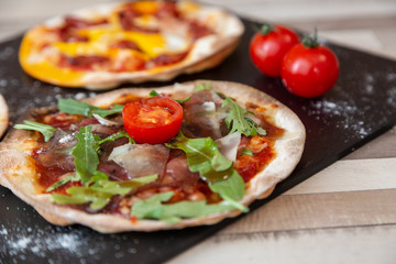 close up of arugula, parmesan, and tomato on a black board garnish with flour on a wooden white table