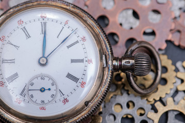 Antique pocket watch and old vintage hour metallic gears on natural stone background.