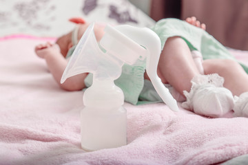 Manual breast pump, mothers breast milk is the most healthy food for newborn baby. Happy mother with baby at background