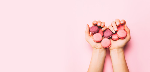 Beautiful female hands with trendy manicure holding pink macaroon cake. Top view, flat lay. Copyspace for your text.