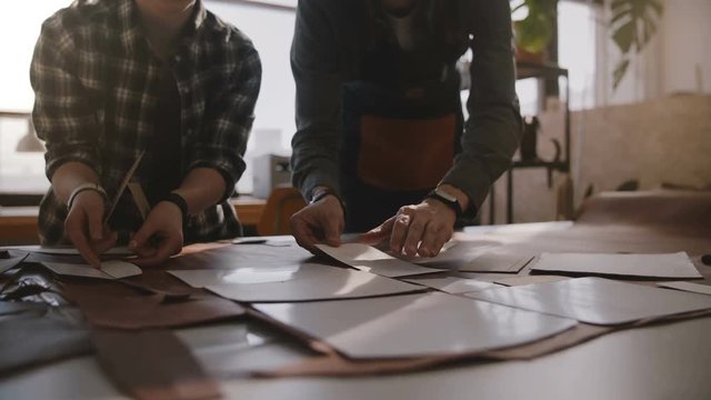 Low angle view of man and woman working together in a manufacture workshop putting cut patterns on big piece of leather.