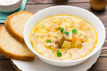 Ready-to-eat chicken soup with potatoes and herbs in a white bowl on a wooden table