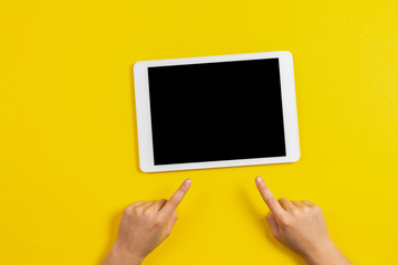 Kid hands finger pointing to tablet computer on yellow background