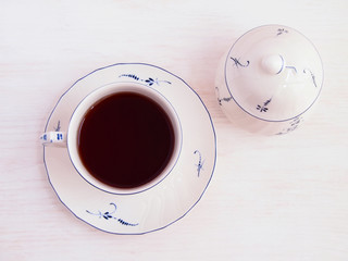 Cup of tea and sugar bowl with blue floral details on wooden background. Top view.