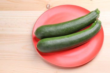 Fresh zucchini on a red plate and wooden background. Healthy food.