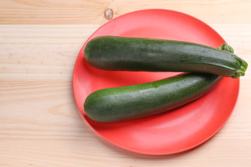 Fresh zucchini on a red plate and wooden background. Healthy food.