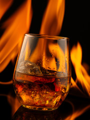 Glass of whiskey with ice on a background of fire.