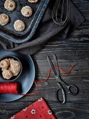 Christmas coconut meringue cookies on baking pan, cookies in black bowl and red ribbon with old scissors. Overhead shot.