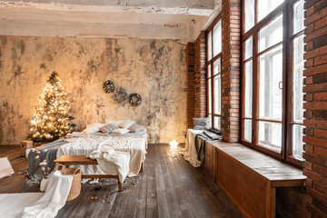 Loft style apartments. Bed in the bedroom, high large Windows. Brick wall with candles and Christmas tree. warm and brown color