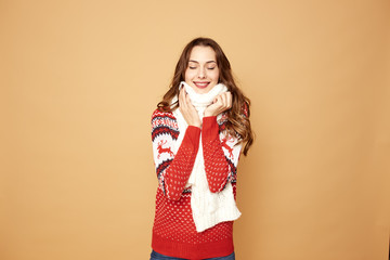 Beautiful girl dressed in a red and white sweater with deer and white knitted scarf stands on a beige background in the studio