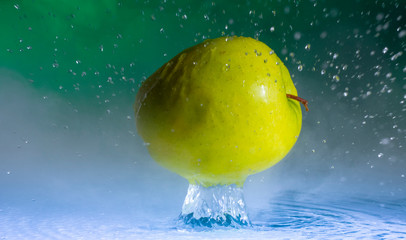 Fototapeta na wymiar Green apple and splashes of water on a colored background
