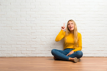 Young girl sitting on the floor intending to realizes the solution while lifting a finger up