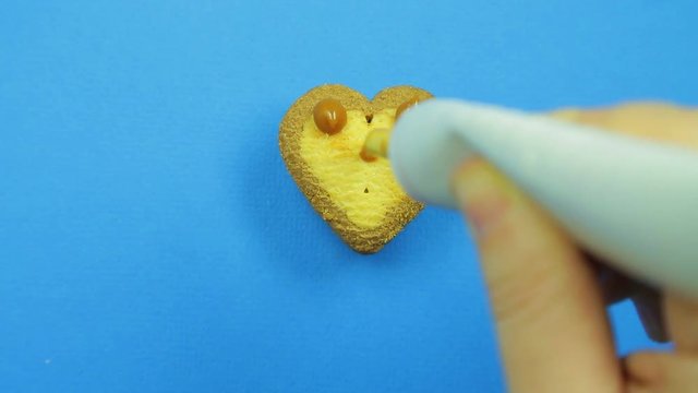 Female hand paints heart-shaped cookies on a blue background with a brown tube icing funny faces.