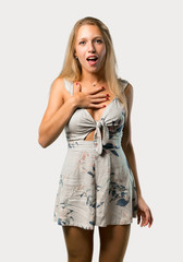 Young blonde woman surprised and shocked while looking right. Expressive facial emotion on grey background