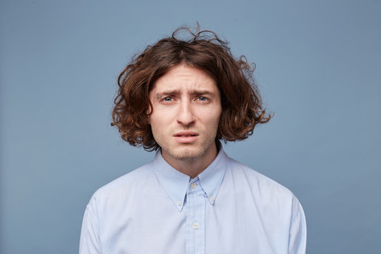 A young man with poor eyesight is trying to make out something, squinting,reading a sign, a focused expression on a blue background.
