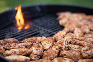 Raw chicken wings grilling on a barbecue, with flames in the background