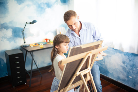 Happy Father's day. Beautiful little girl with her father to paint and draw picture art  with watercolor on Easel happily at her home, education, activities family love and lifestyle concept.