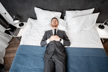 Businessman in the suit lying on the bed like a dead man at the hotel room or bedroom