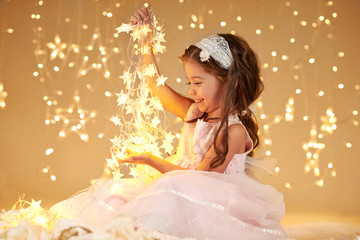 girl child is playing with christmas lights, yellow background, pink dress © soleg