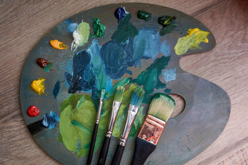 Artist palette with oil paints and brushes on a wooden background.