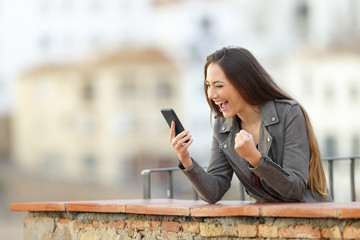 Excited woman checking smart phone in a balcony