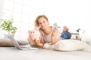 Young woman smiling holding credit card and piggy bank, using laptop computer, online shopping...
