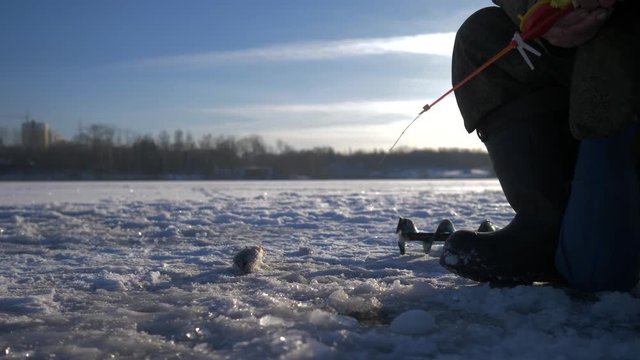 An old man fisherman fishing in the winter on the lake. Winter fishing. Winter ice fishing. 4K