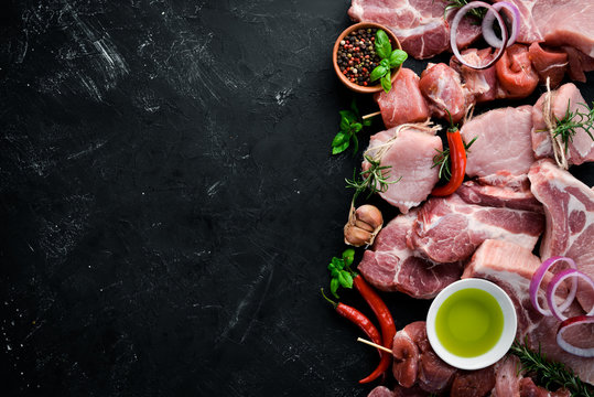 Raw meat for barbecue. Meat with spices and herbs. On a black stone background. Top view. Free copy space.