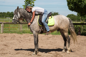 Reiterin umarmt ihr Pferd (Schimmel)