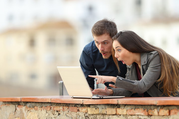 Surprised couple checking laptop content in a balcony