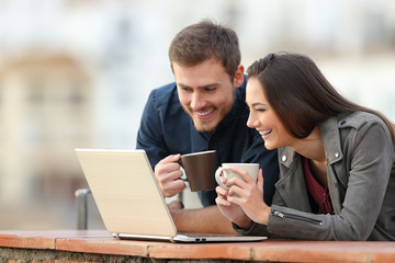 Happy couple checking laptop content on a balcony
