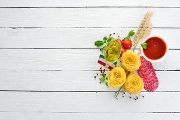 Dry pasta. Pasta and fresh vegetables. Top view. On a white wooden background. Free copy space.