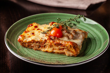 The concept of Italian cuisine. Baked lasagna with minced bolognese, pasta, cherry tomatoes lies on a green plate in a restaurant. A glass of red wine and bread basket on the table