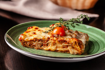 The concept of Italian cuisine. Baked lasagna with minced bolognese, pasta, cherry tomatoes lies on a green plate in a restaurant. A glass of red wine and bread basket on the table