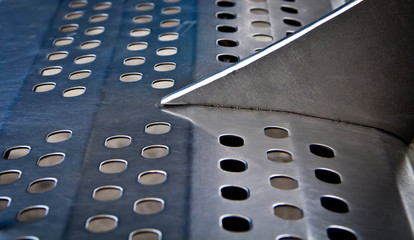 Perforated metal texture with circular pattern—urban surface detail from a train station bench,...