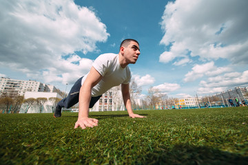 Fitness man plank workout training in park outdoors. Young guy makes exercise. Healthy lifestyle, gymnastics concept