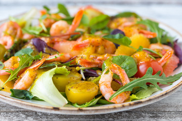 salad with shrimps and assorted salads (arugula, cherry tomatoes, chard, spinach) on white wooden background