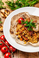 The concept of Eastern, Turkish, Uzbek cuisine. Pilaf with pieces of meat is served in pita bread, in a white plate on a wooden table. parsley and vegetables on the table.
