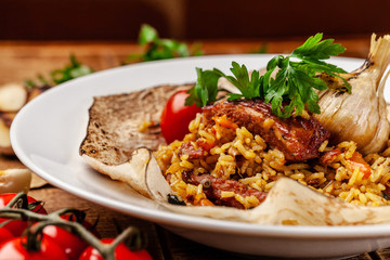 The concept of Eastern, Turkish, Uzbek cuisine. Pilaf with pieces of meat is served in pita bread, in a white plate on a wooden table. parsley and vegetables on the table.