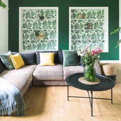 Stylish and modern interior with sofa, colors pillows, flowers and wooden floor. Sunny and bright...