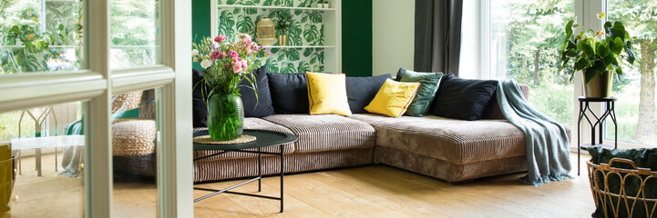 Modern and cozy living room with corduroy sofa, colors pillows, big window to the garden. Bright...