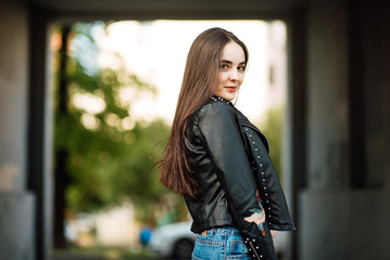 Portrait young punk rock fashion girl in a black leather jacket with stilettos in an urban environment of a street warehouse, woman in jeans walking